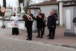 grupa mężczyzn niosących kwiaty pod pomnik