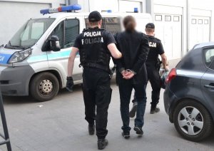 umundurowani policjanci prowadzą zatrzymanego na parkingu policyjnym