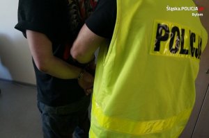 policjant w kamizelce policyjnej zakłada zatrzymanemu kajdanki
