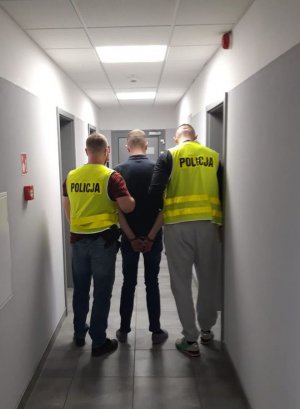 dwaj policjanci prowadza zatrzymanego mężczyznę