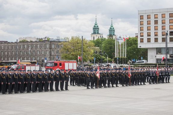 strażacy stojący w szeregu na Pl. Piłsudskiego w Warszawie podczas centralnych obchodów dnia strażaka, w tle wozy strażackie