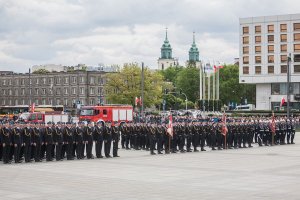 funkcjonariusze PSP stojący w szeregu na Pl. Piłsudskiego w Warszawie podczas centralnych obchodów święta strażaka, w tle widać wozy straży pożarnej