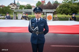 policjantka w nowym umundurowaniu stojąca przy wielkiej fladze Polski podczas defilady