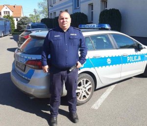 Funkcjonariusz z Komisariatu Policji w Nowogardzie w mundurze na tle radiowozu