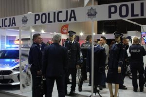 Na stoisku policyjnym, na manekinach prezentowane są nowe mundury galowe: mundur kobiecy, mundur męski, płaszcz oficerski. Stoiskiem zainteresowana jest grupa ludzi.
