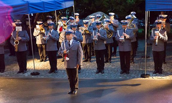 orkiestra policyjna stoi przed budynkiem Komendy Głównej Policji w szeregach i gra na instrumentach