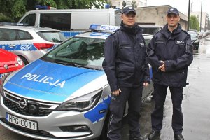 dwaj dzielnicowi w mundurach, którzy udzielili pomocy mężczyźnie. W tle radiowozy policyjne i prywatne samochody
