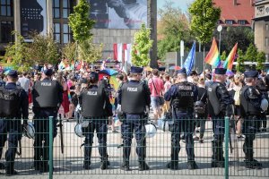 Policjanci Oddziału Prewencji Policji stoją w równych odległościach wzdłuż torowiska tramwajowego. Obserwują uczestników „Marszu Równości” zbierających się przy Muzeum Narodowym w Krakowie.