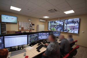 Centrum monitoringu Urzędu Miasta. W sali znajduje się kilkanaście monitorów oraz jeden zbiorczy, powieszony na ścianie. Kilka osób obserwuje monitoring miejski.