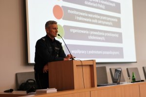 Policjant przemawia do uczestników konferencji stojąc za mównicą