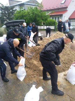 grupa policjantów nasypuje piasek do worków