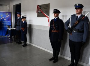 Zdjęcie w kolorze. Na pierwszym planie tablica upamiętniająca podinspektora Romana Prota Sztabę, a także asysta policjantów w mundurach obecnych oraz z okresu II RP.