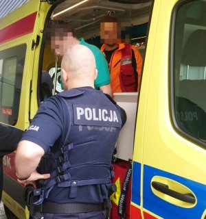 zatrzymany mężczyzna wysiada z karetki pogotowia w asyście policjanta i ratownika medycznego