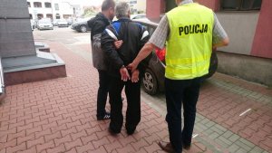 dwaj policjanci prowadzą zatrzymanego mężczyznę do radiowozu