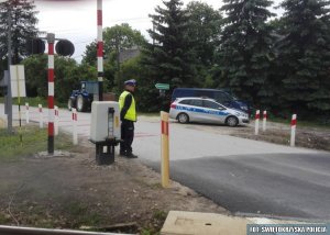 policjant stoi na przejściu kolejowym w tle traktor oraz radiowóz policyjny  oraz bus