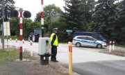 policjant stoi na przejściu kolejowym w tle traktor oraz radiowóz policyjny  oraz bus