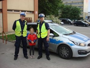 Na zdjęciu widoczni są dwaj policjanci Wydziału Ruchu Drogowego z małą dziewczynką w wieku 8 lat ubraną w koszulkę reprezentacji Polski. Wszyscy pozują do zdjecia