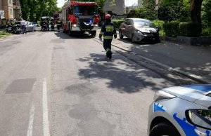 dwa rozbite samochody i wóz strażacki oraz strażacy pracujący na miejscu wypadku