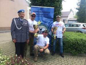 czterej weterani, trzej z nich trzyma puchary jeden z nich ubrany w strój galowy, w tle baner stowarzyszenie weteranów działań poza granicami rp