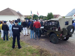 Umundurowana policjantka stoi obok zabytkowego samochodu wojskowego, na drugim planie tłum ludzi