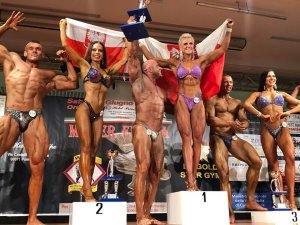 zawodnicy fitness na podium trzymają polską flagę