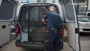 policjant zamyka drzwi radiowozu policyjnego, w którym siedzi zatrzymany mężczyzna