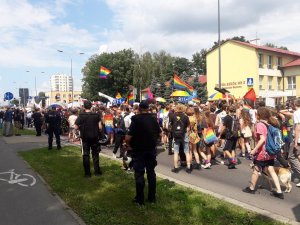 uczestnicy marszu idą ulicami miasta z flagami policjanci stoją i pilnują porządku