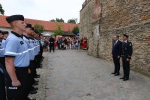 funkcjonariusz czeskiej Policji stoi z prawej strony razem z mężczyzną w garniturze. Na przeciwko nich w dwuszeregu stoją czescy policjanci. Z tyłu stoją goście, którzy przyglądają się uroczystości