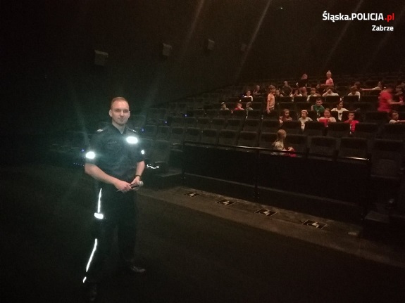 Policjant wspólnie z dziećmi w sali kinowej.