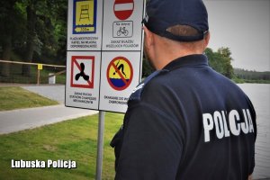 policjant nad jeziorem stoi przy tablicy informacyjnej