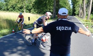 sędzia kieruje jadących na rowerach kolarzy