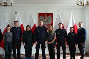 litewscy oraz polscy policjanci w Komendzie Głównej Policji pozują do zdjęcia  w tle godło Polski oraz flagi