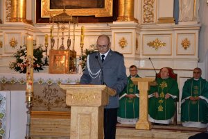 Przy ołtarzu policjant w umundurowaniu galowym czyta, stojąc przy małej ambonie