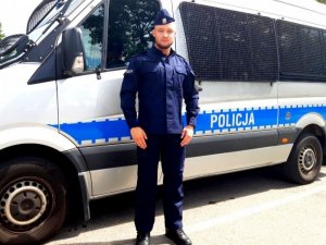 Policjant który uratował 14-latkę stojący na tle radiowozu.