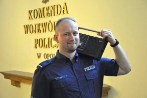Tomasz Lis stoi na tle napisu komendy wojewódzkiej i trzyma oparty na ramieniu radioodtwarzacz starego typu