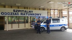 dwaj policjanci stoją obok radiowozu, który stoi obok szpitala