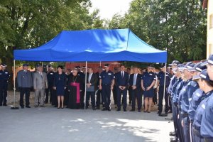 Umundurowani policjanci stojący w szeregu oraz osoby cywilne stojące pod namiotem