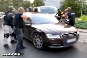 Dynamiczne zatrzymanie w miejscu publicznym. Policjanci otaczają  auto osoby podejrzanej.