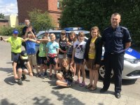 policjant z młodzieżą stoją przy radiowozie