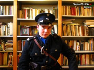 Na zdjęciu znajduje się policjant w mundurze Policji Województwa Śląskiego. W tle widać biblioteczkę.