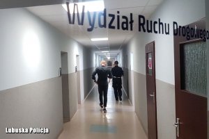 Na zdjęciu widać mężczyznę i policjantkę idący korytarzem.