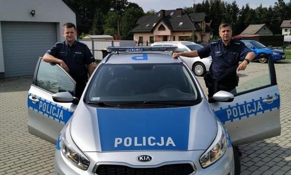 dwaj policjanci stoją przy radiowozie poicyjnym