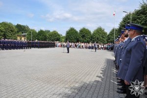 Plac, wokół którego stoją policjanci oraz zaproszeni goście uroczystości na środku stoi przy mikrofonie i przemawia