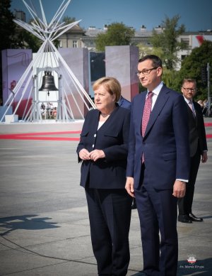 Kanlcerz Angela Merkel i Premier RP Mateusz Morawiecki - stoją obok siebie, w tle dzwoń Pamięć i przestroga