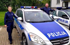 Fotografia kolorowa przedstawiająca dwoje policjantów stojących przy radiowozie