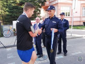 policjant wręcza medal kolejnemu uczestnikowi biegu, który dotarł na metę