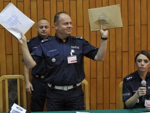 Na zdjęciu widnieje policjant trzymający koperty z testami w rękach.