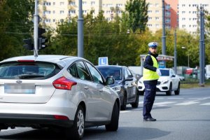 policjant kieruje ruchem drogowym, na pierwszym planie auto osobowe