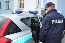 Zdjęcie ilustracyjne, na którym umundurowany Policjant umieszcza zatrzymanego mężczyznę w oznakowanym radiowozie
