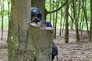 Policjant opiera karabin o pień drzewa.